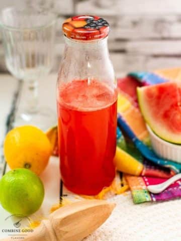 Preserving bottle filled with vibrant watermelon syrup placed on white wooden ground.