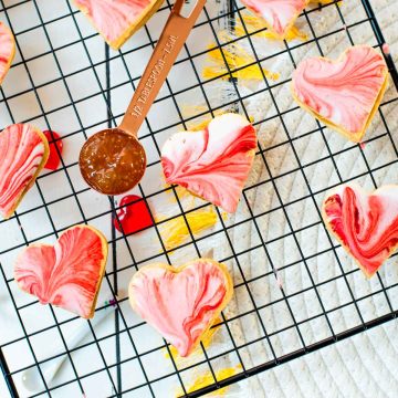 Gorgeous heart shaped sugar cookies with marbled icing, and filled with fig jam. Placed on cooling rack next to half a tablespoon of fig jam.