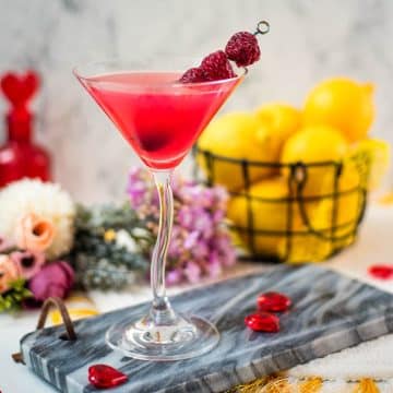 Cocktail glass filled with delicious raspberry lemon drop martini and garnished with raspberries on a cocktail spike.