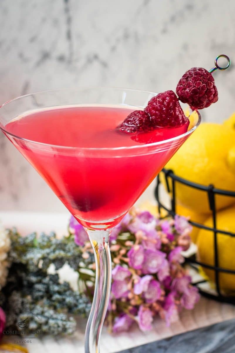 Cocktail glass filled with delicious raspberry lemon drop martini and garnished with raspberries on a cocktail spike.