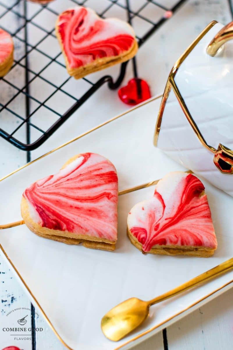 Gorgeous heart shaped sugar cookies with marbled icing, and filled with fig jam. Placed on gorgeous white golden serving plate.