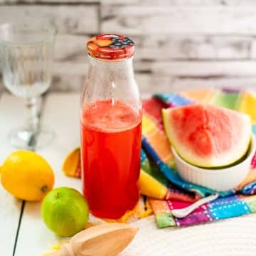 Preserving bottle filled with vibrant watermelon syrup placed on white wooden ground.