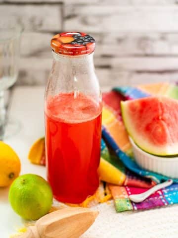 Preserving bottle filled with vibrant watermelon syrup placed on white wooden ground.