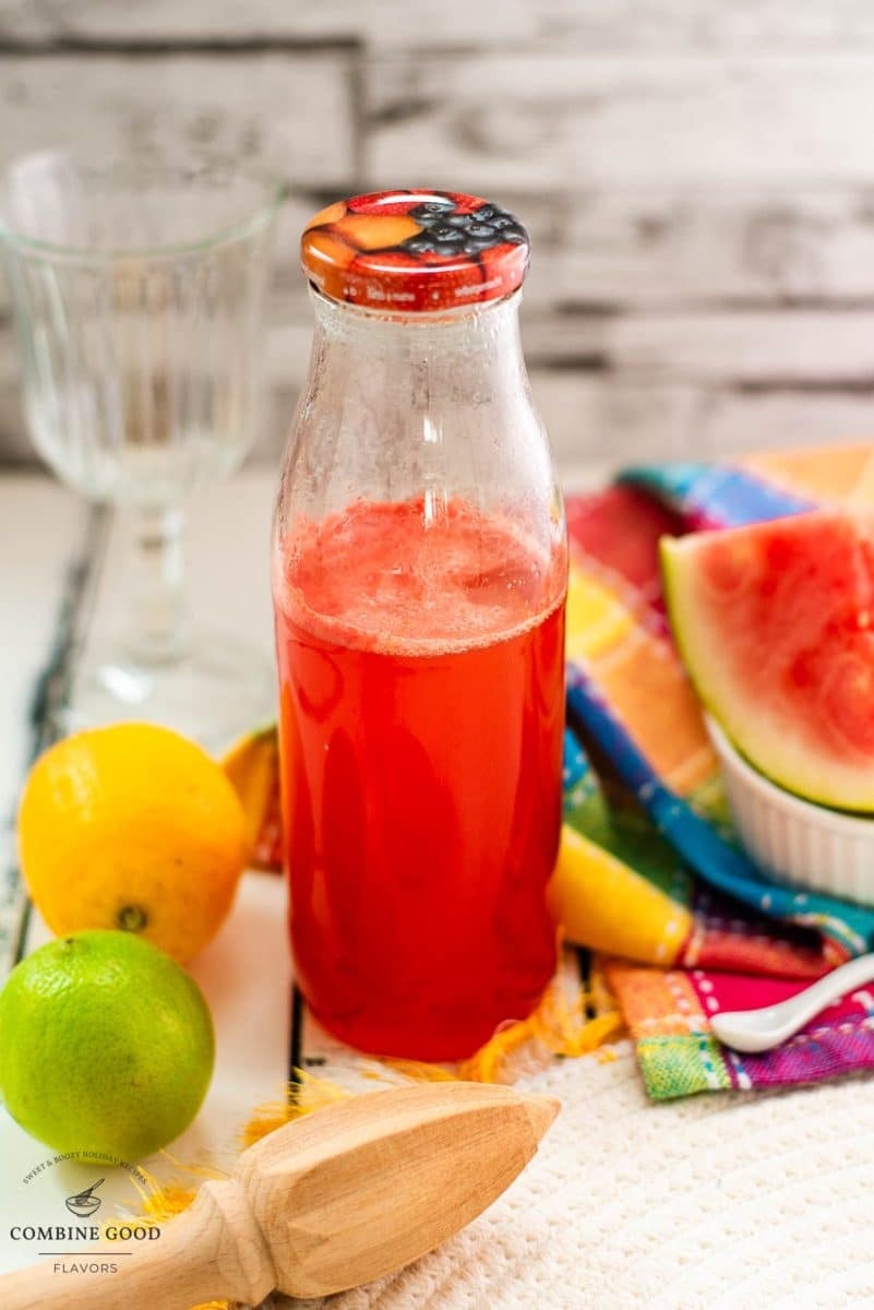 Preserving bottle filled with vibrant watermelon syrup placed on white wooden ground.