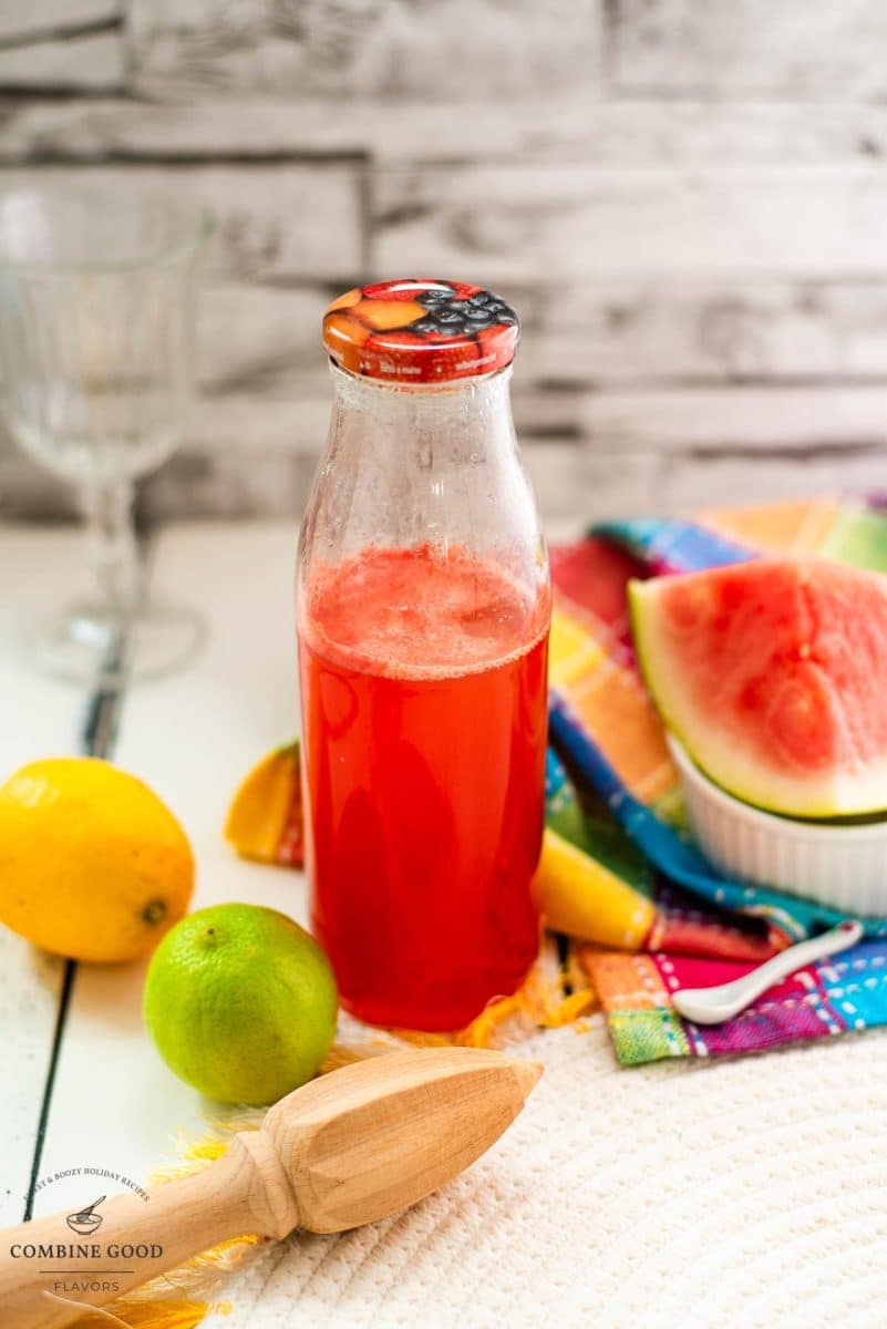 Preserving bottle filled with vibrant watermelon syrup placed on white wooden ground.