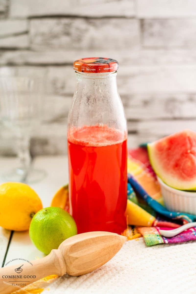 Preserving bottle filled with vibrant watermelon syrup placed on white wooden ground.