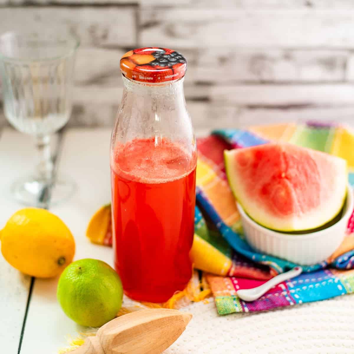 Preserving bottle filled with vibrant watermelon syrup placed on white wooden ground.