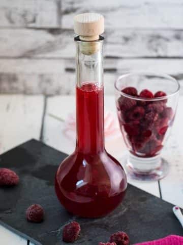 Flask filled with homemade raspberry syrup, placed on a black slate plate.