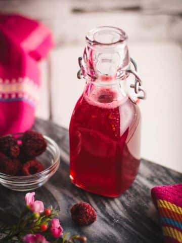 Preserving bottle, filled with delicious uncooked raspberry syrup placed on a marbled plate.