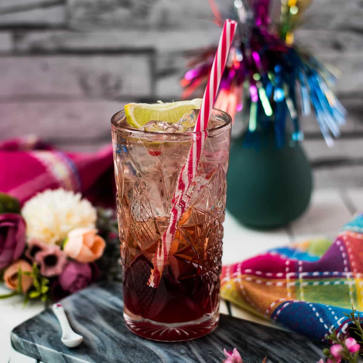 Gorgeous high ball glass filled with raspberry gin tonic, using sloe gin. Garnished with a lime wedge and a drinking straw.