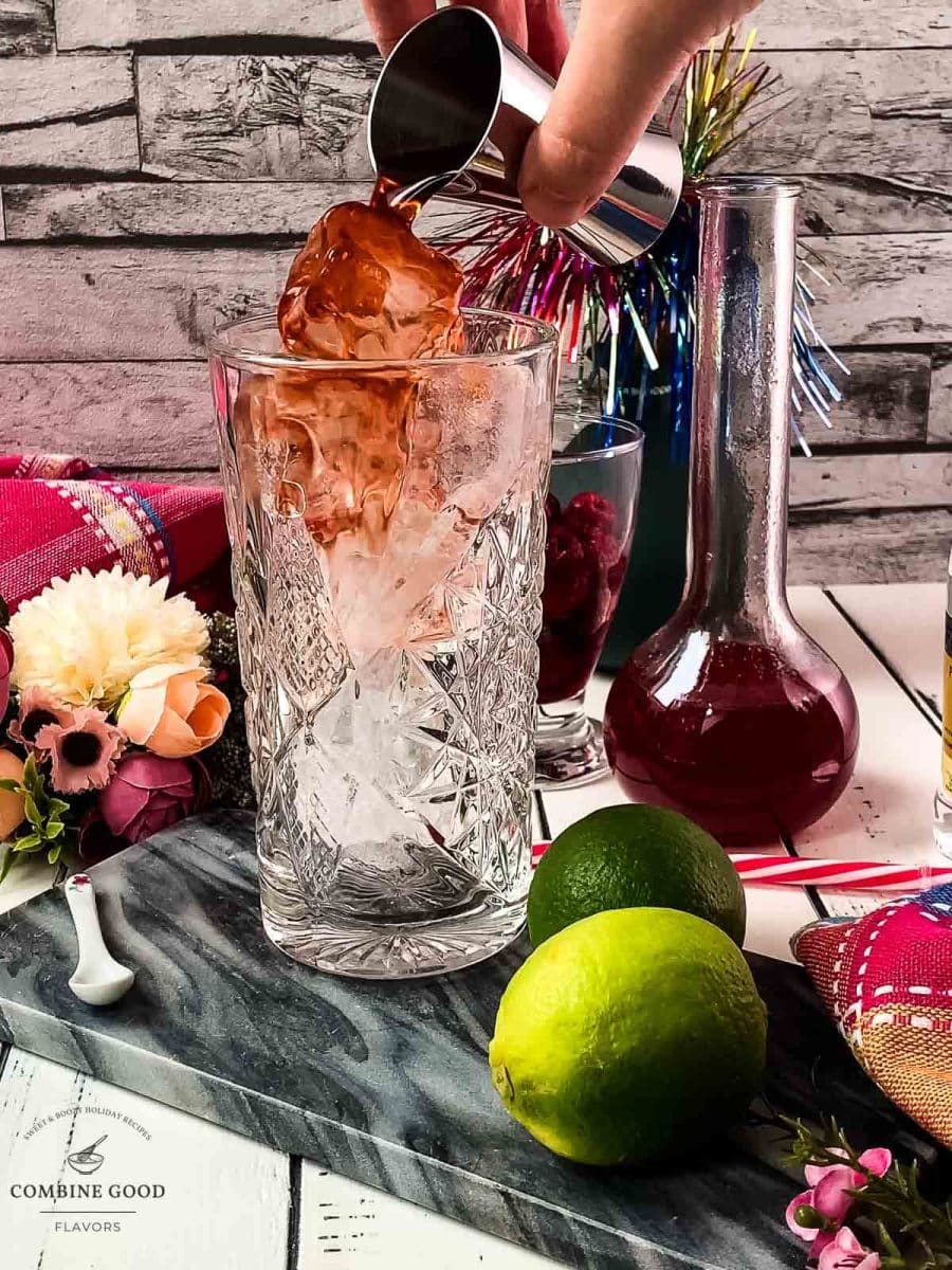 Pouring the sloe gin over the cubed ice into a highball glass.