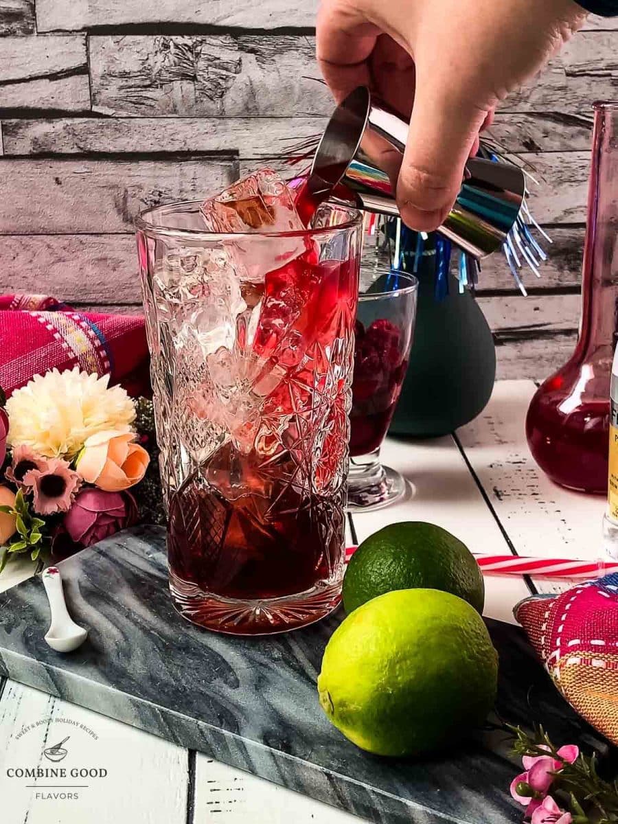 Pouring raspberry syrup over the cubed ice into a highball glass.