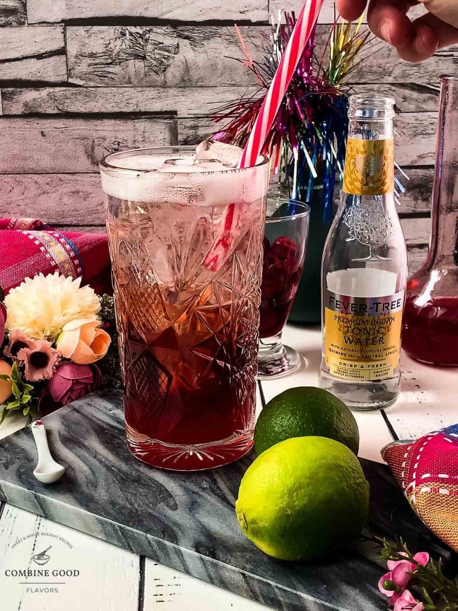 Placing a red and white drinking straw into the raspberry gin and tonic.