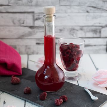 Flask filled with homemade raspberry syrup, placed on a black slate plate.