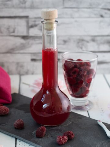 Flask filled with homemade raspberry syrup, placed on a black slate plate.