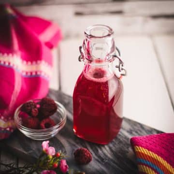 Preserving bottle, filled with delicious uncooked raspberry syrup placed on a marbled plate.