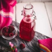Preserving bottle, filled with delicious uncooked raspberry syrup placed on a marbled plate.