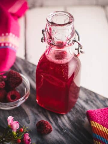 Preserving bottle, filled with delicious uncooked raspberry syrup placed on a marbled plate.