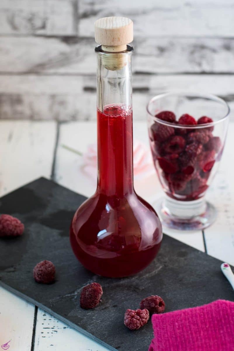 Flask filled with homemade raspberry syrup, placed on a black slate plate.