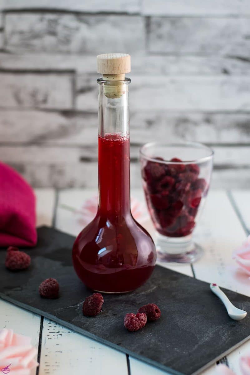 Flask filled with homemade raspberry syrup, placed on a black slate plate.