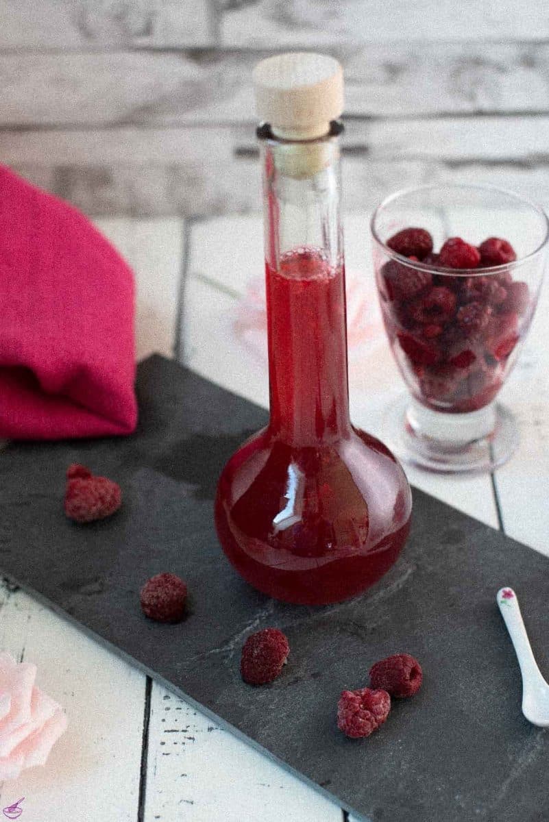 Flask filled with homemade raspberry syrup, placed on a black slate plate.