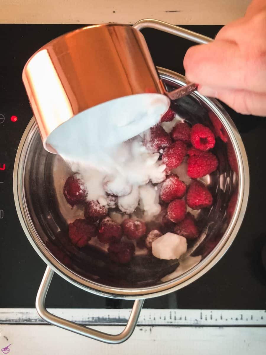 Pouring sugar into a saucepan filled with water and fresh raspberries.