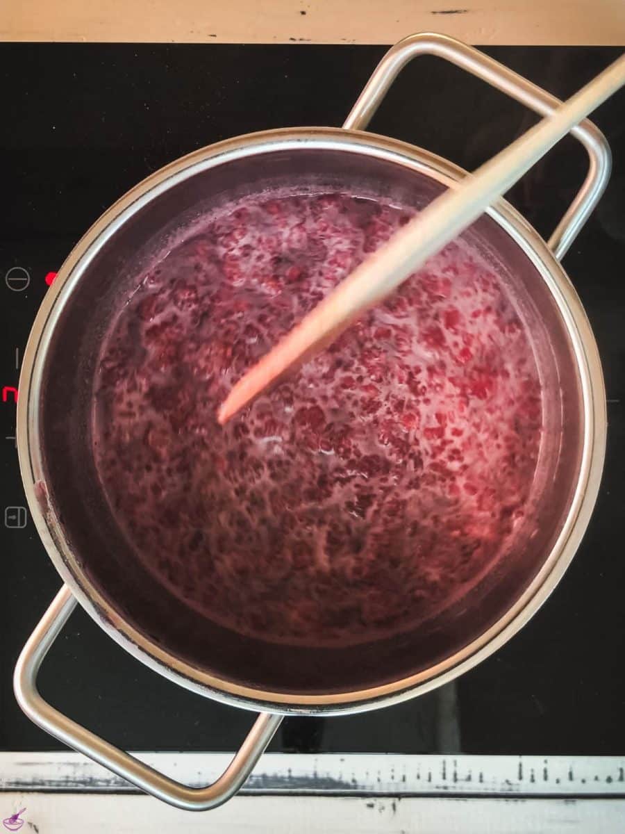 Saucepan filled with raspberry sauce with a wooden spoon across.