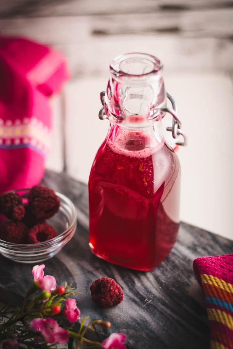 Preserving bottle, filled with delicious uncooked raspberry syrup placed on a marbled plate.