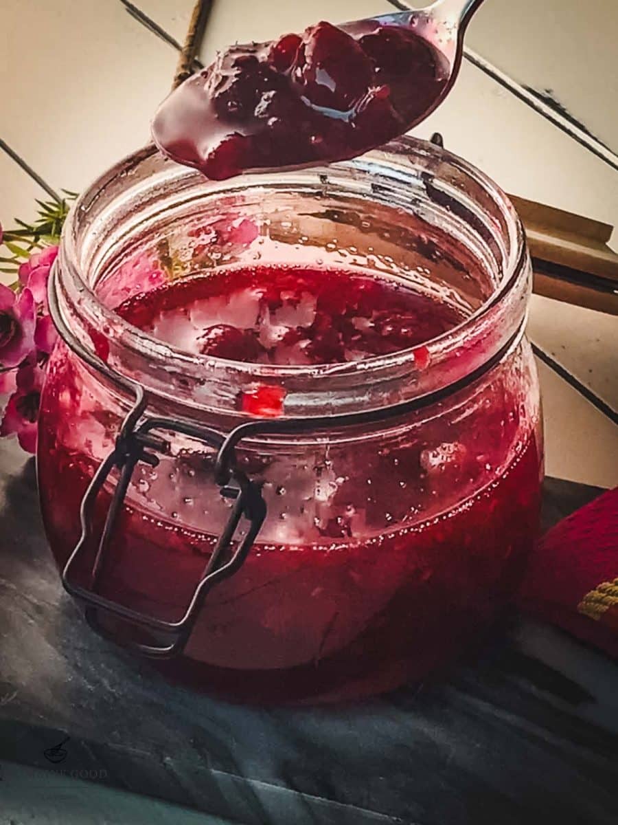 Spoon with raspberry sauce hovering over a preserving jar filled with raspberry sauce.