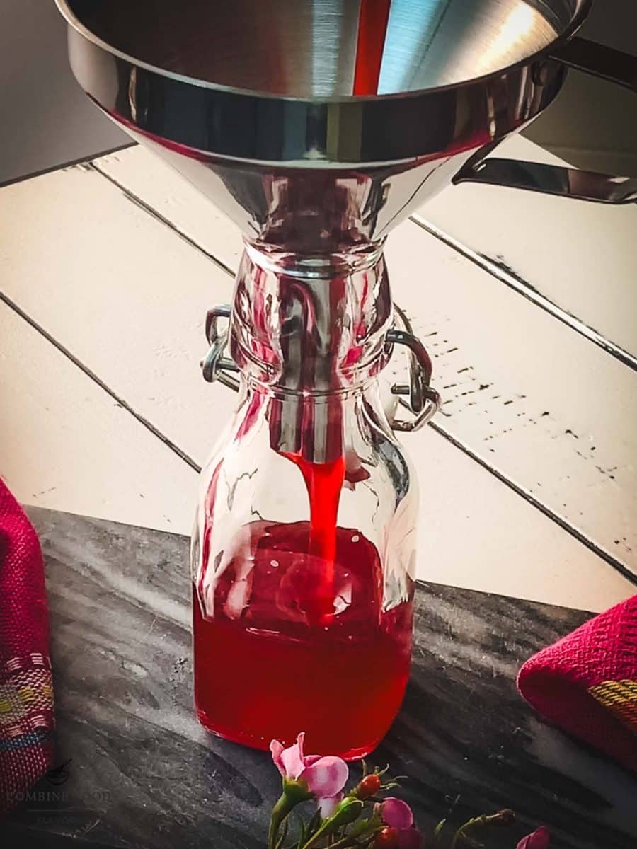 Pouring the finished raspberry syrup into a preserving bottle using a funnel.