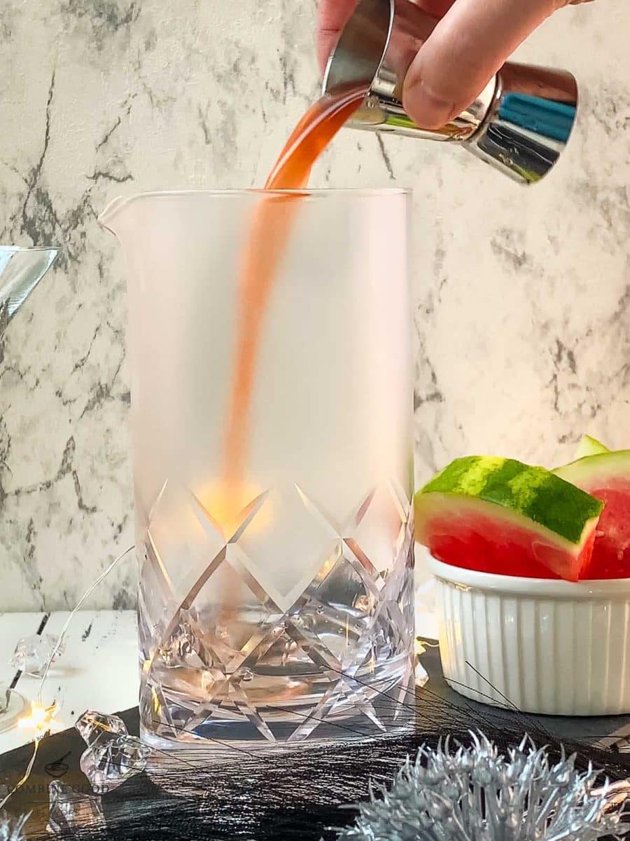 Adding homemade watermelon syrup into the stirring glass.