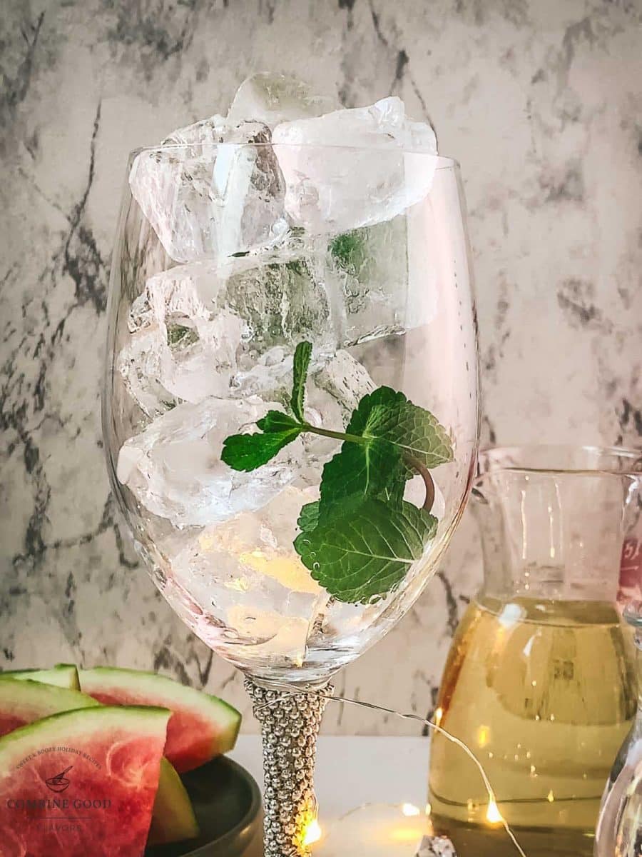 Adding cubed ice and mint leaves to the wine glass.