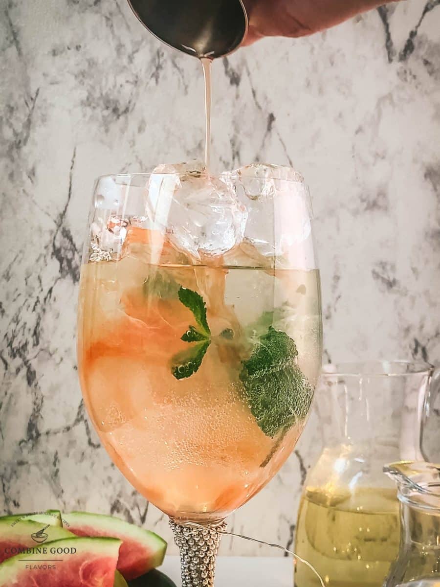 Adding watermelon syrup to the wine glass using a jigger.