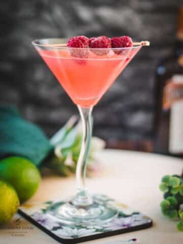 Delicious raspberry margarita served in cocktail glass and garnished with fresh raspberries on a cocktail spike.