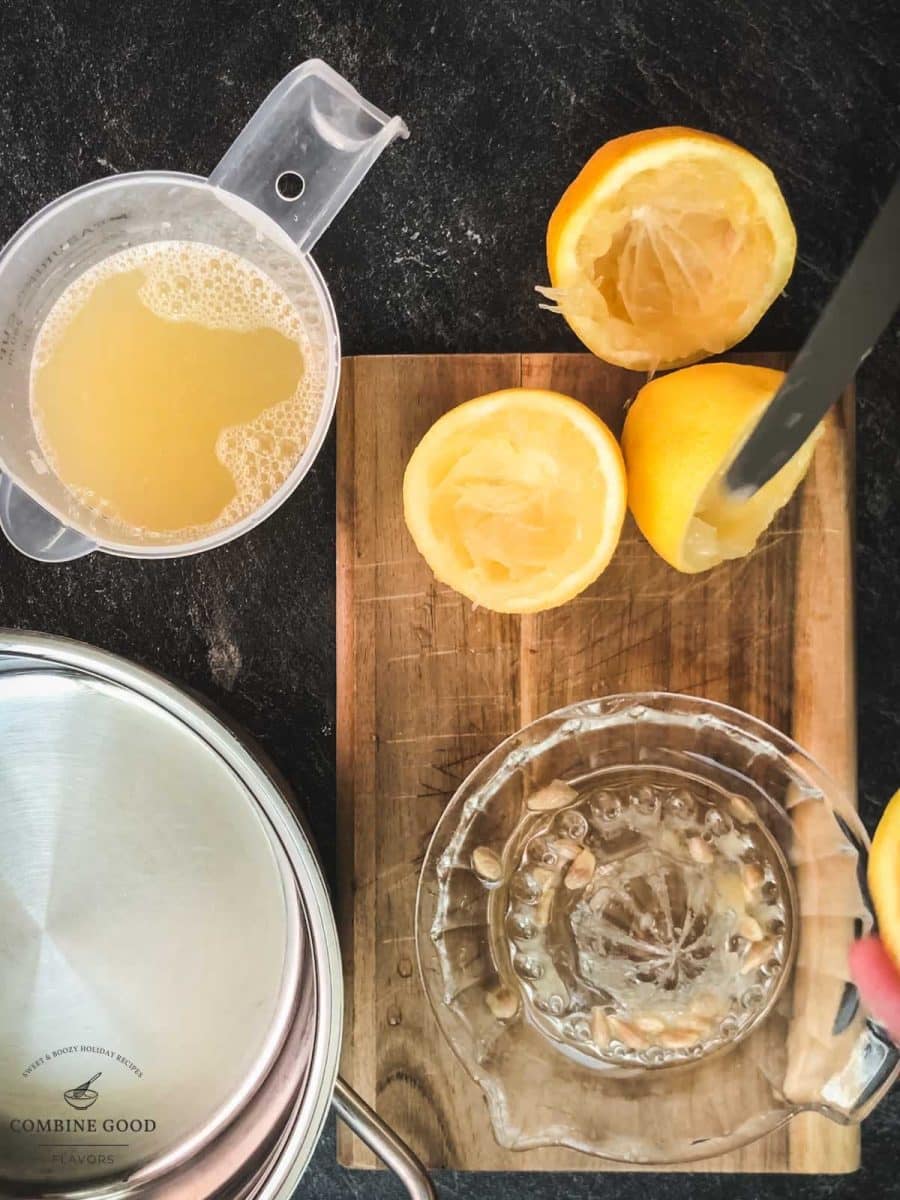 Wooden chopping board next to lemons, lemon juice and lemon squeezer.