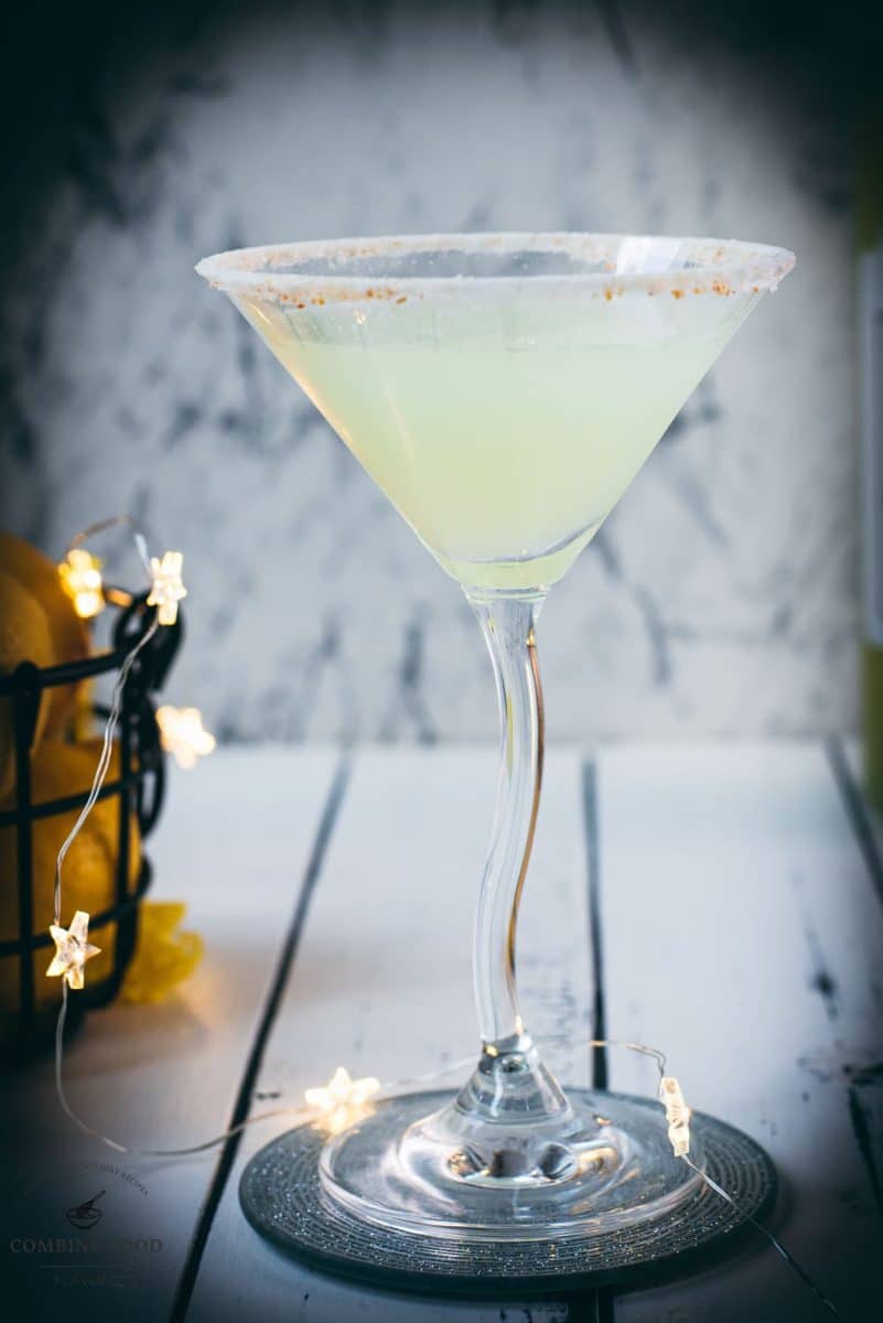 Gorgeous Limoncello vodka martini with orange sugar rim, placed on a mirrored coaster on a white wooden board.