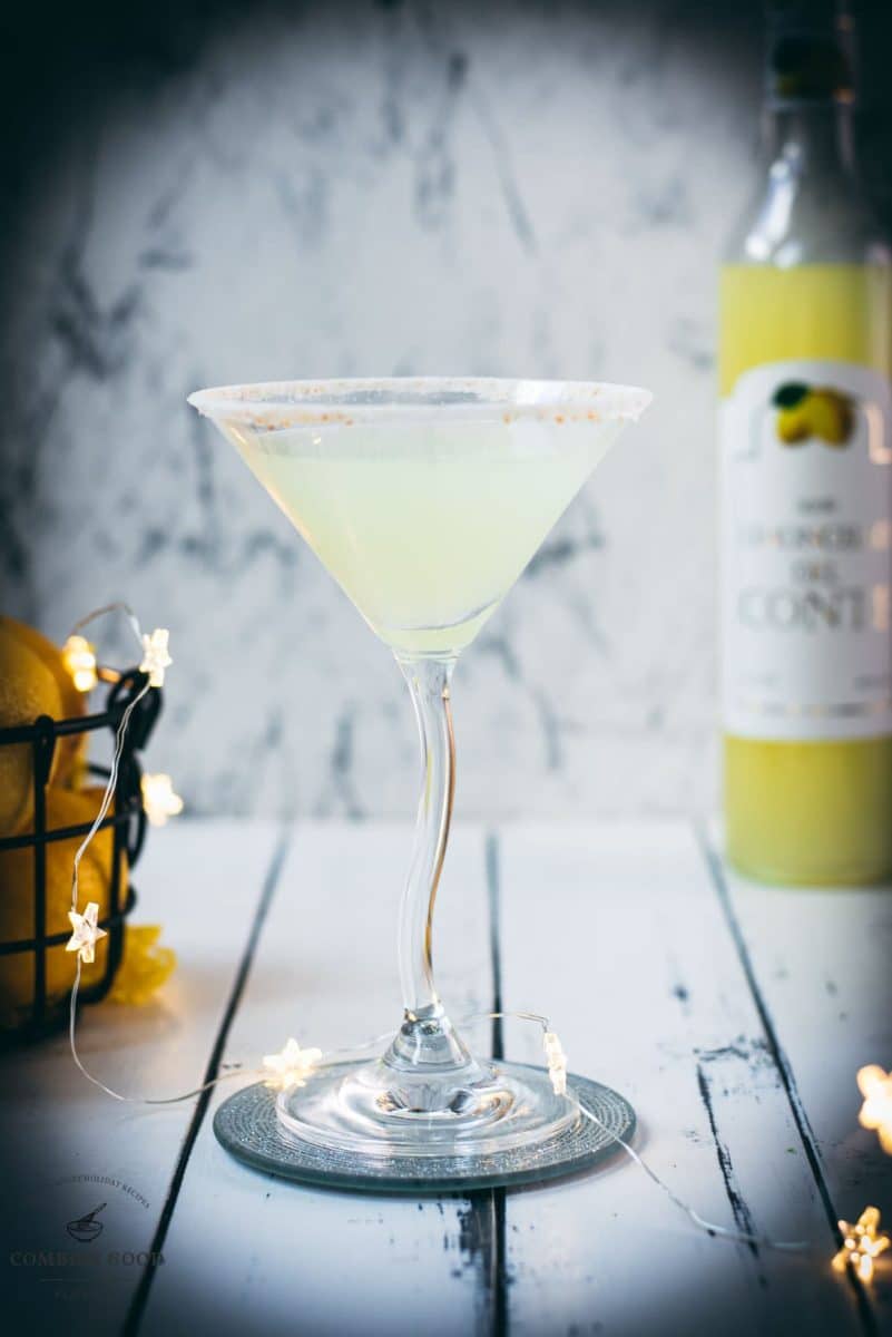 Gorgeous Limoncello vodka martini with orange sugar rim, placed on a mirrored coaster on a white wooden board.