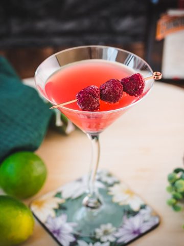 Delicious raspberry margarita served in cocktail glass and garnished with fresh raspberries on a cocktail spike.