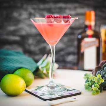 Delicious raspberry margarita served in cocktail glass and garnished with fresh raspberries on a cocktail spike.