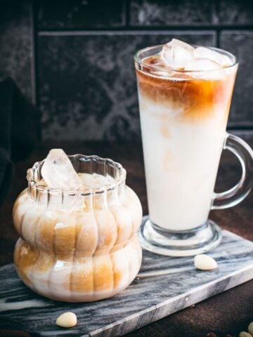 Glasses filled with delicious iced almond milk latte, placed on marbled plate.