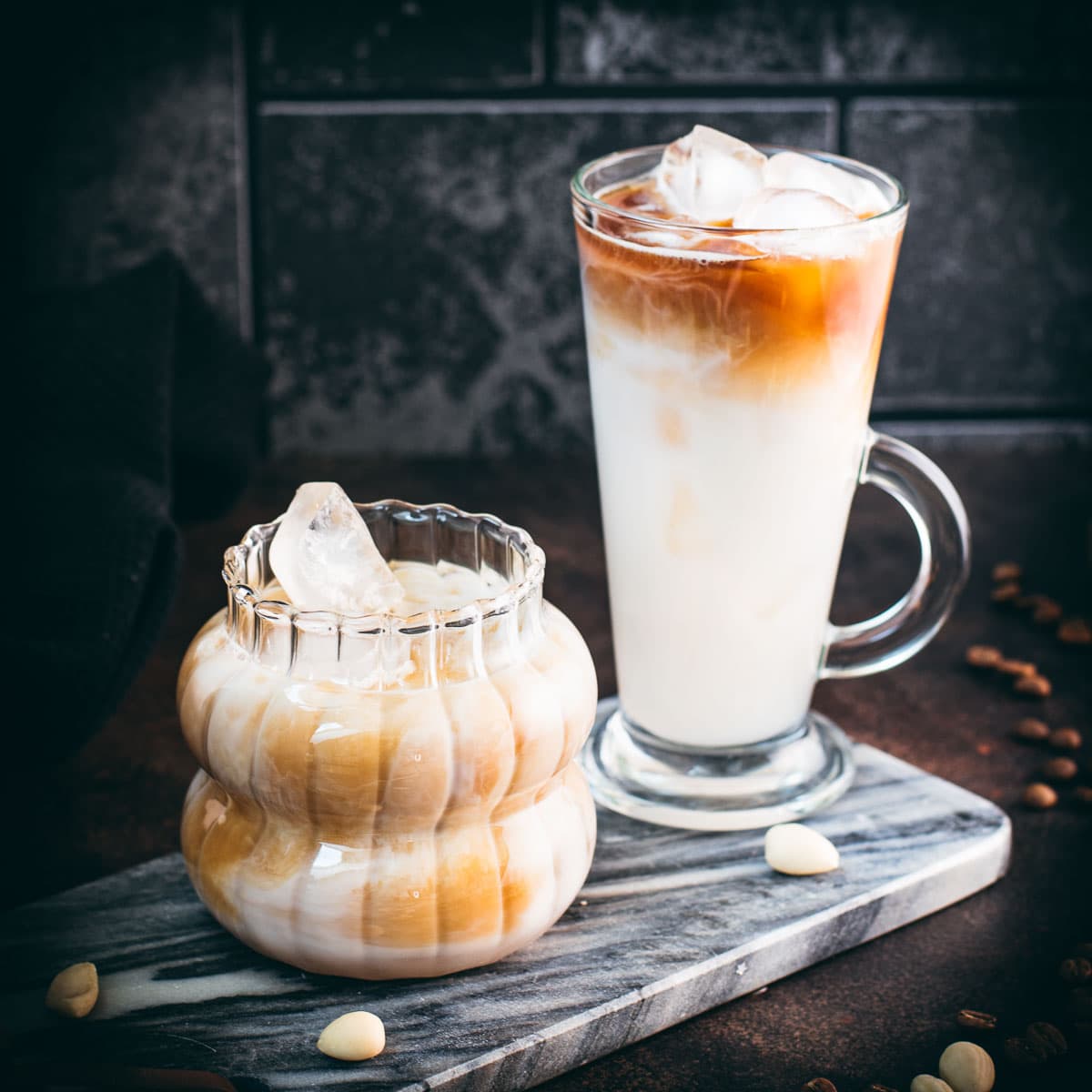 Glasses filled with delicious iced almond milk latte, placed on marbled plate.