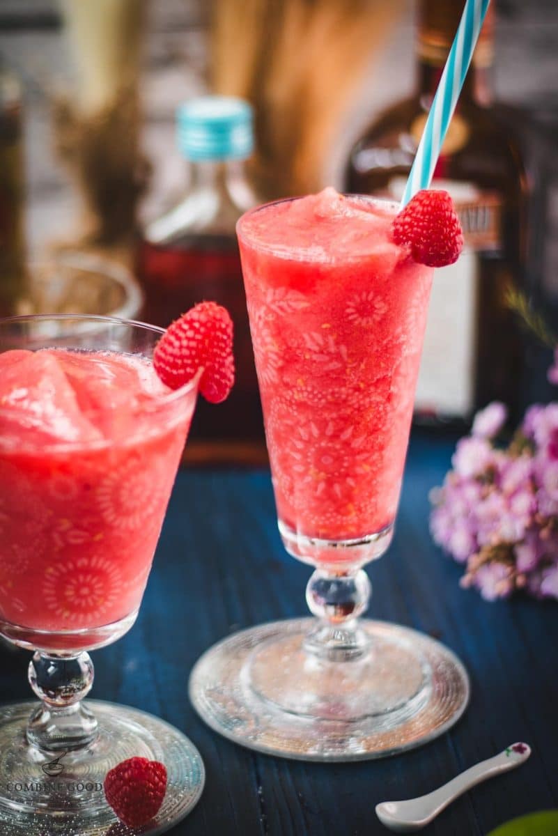 Two gorgeous glasses filled with a delicious frozen raspberry margarita cocktail, placed on glass coaster.