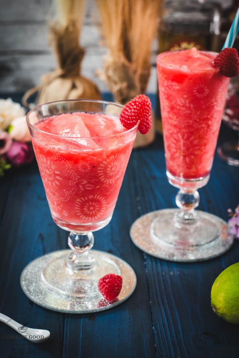 Two gorgeous glasses filled with a delicious frozen raspberry margarita cocktail, placed on glass coaster.