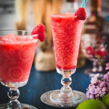 Two gorgeous glasses filled with a delicious frozen raspberry margarita cocktail, placed on glass coaster.