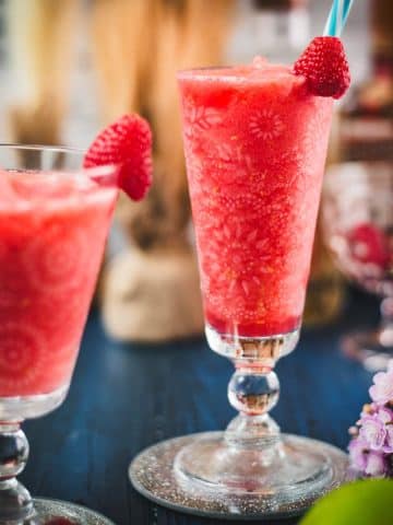 Two gorgeous glasses filled with a delicious frozen raspberry margarita cocktail, placed on glass coaster.