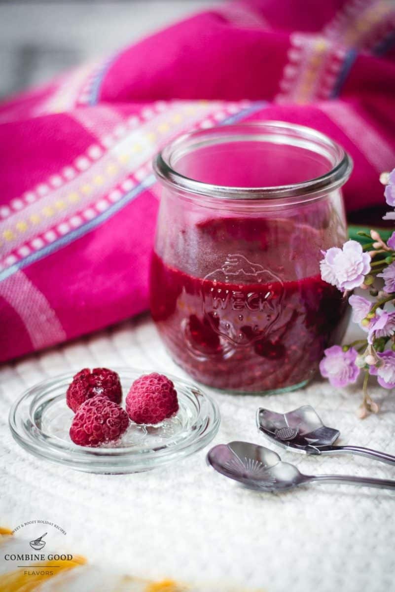 Vibrant raspberry cheesecake topping in a preserving jar, placed on white structured ground.