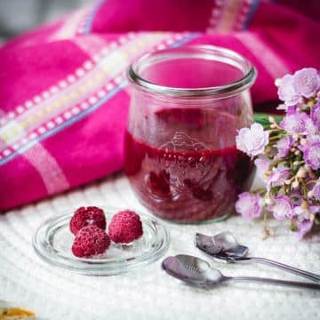 Vibrant raspberry cheesecake topping in a preserving jar, placed on white structured ground.