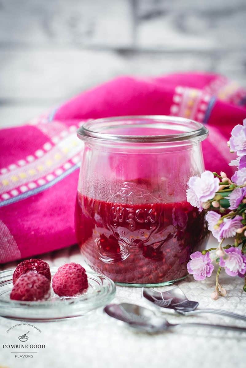 Vibrant raspberry cheesecake topping in a preserving jar, placed on white structured ground.