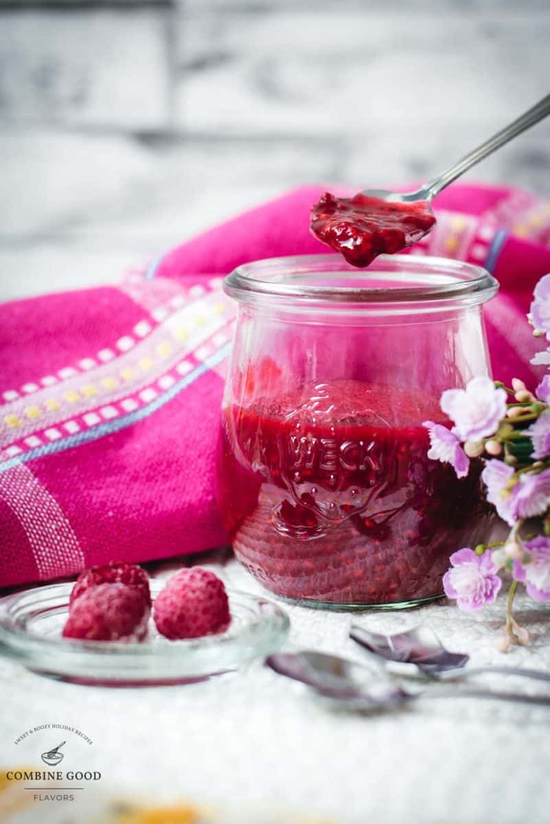 Vibrant raspberry cheesecake topping in a preserving jar, placed on white structured ground.