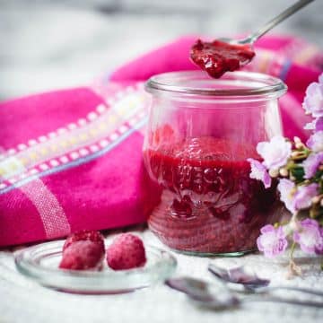 Vibrant raspberry cheesecake topping in a preserving jar, placed on white structured ground.